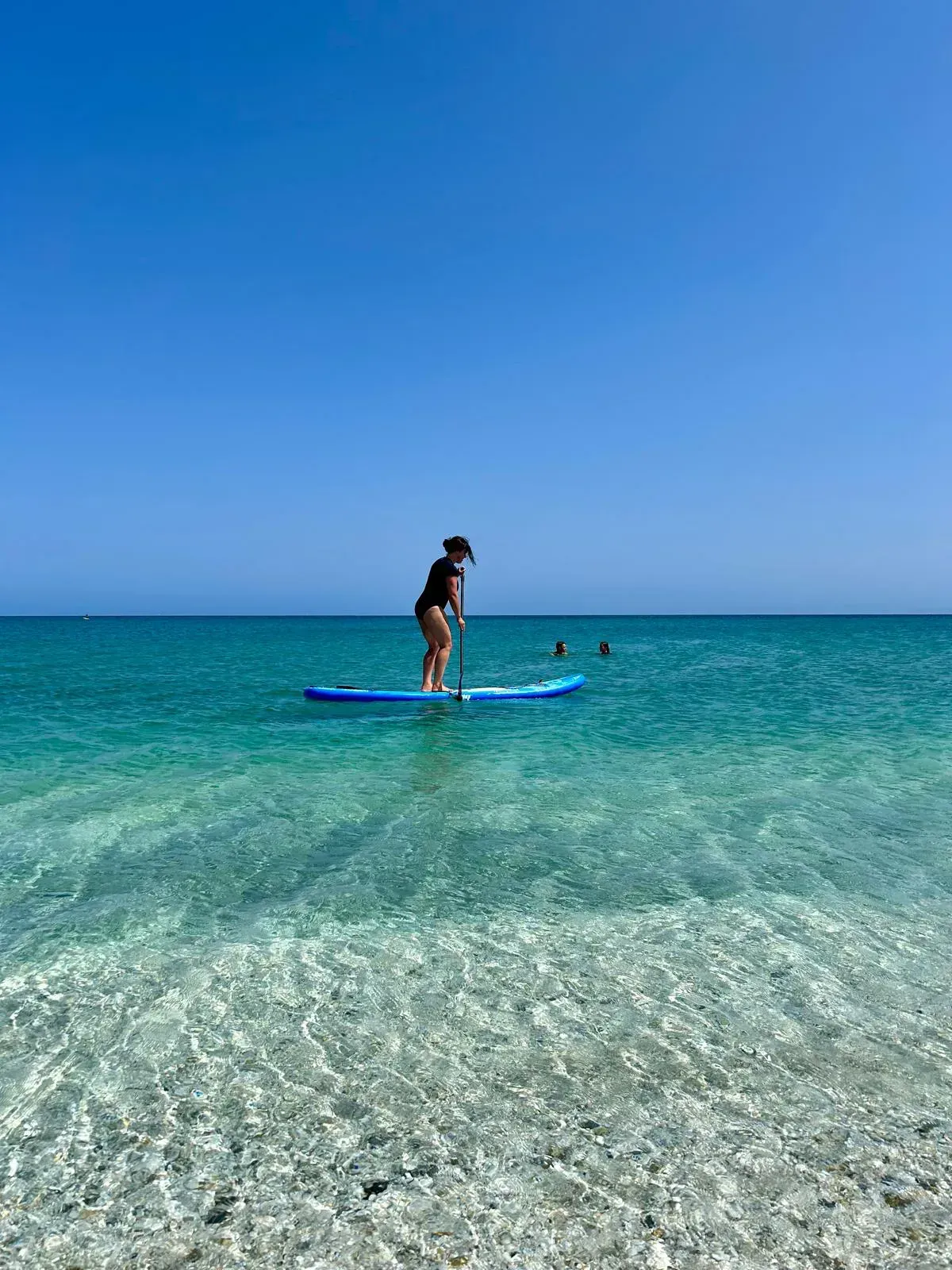 Eine Frau steht auf einem Paddelbrett im Meer.
