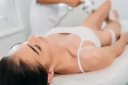 Dona rebent tractament corporal en un llit blanc, tècnic utilitza un dispositiu a la cama.