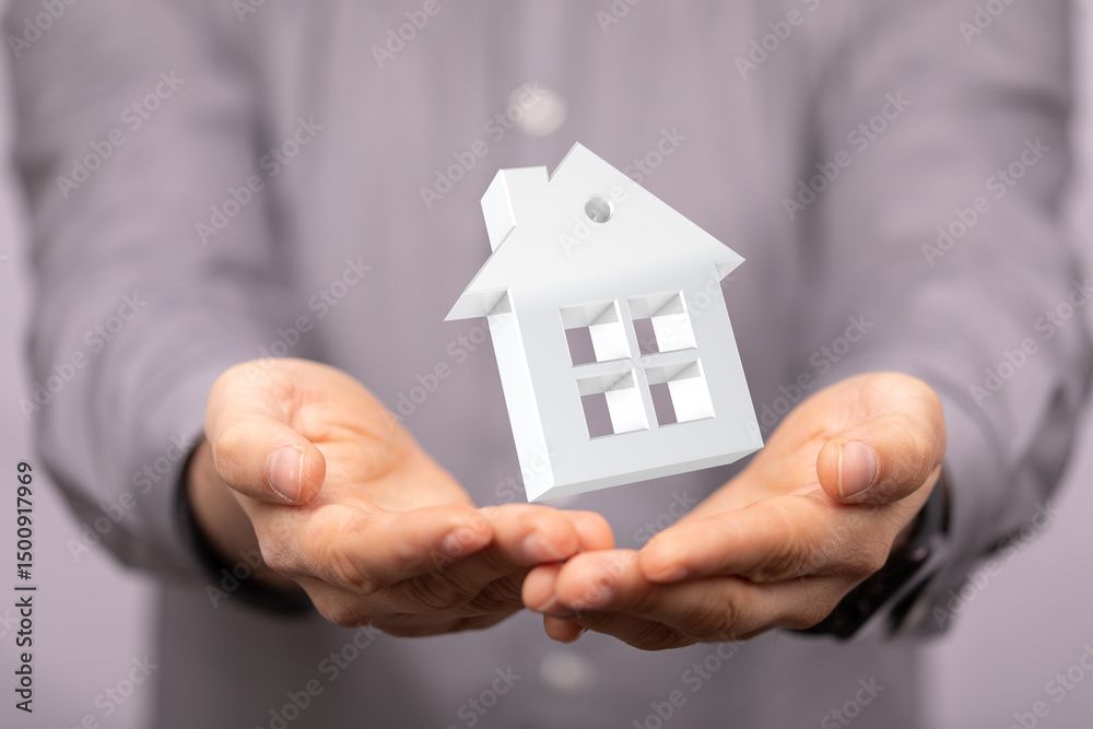 Personne tenant une petite maison blanche, symbolisant la propriété ou la propriété d'une maison.