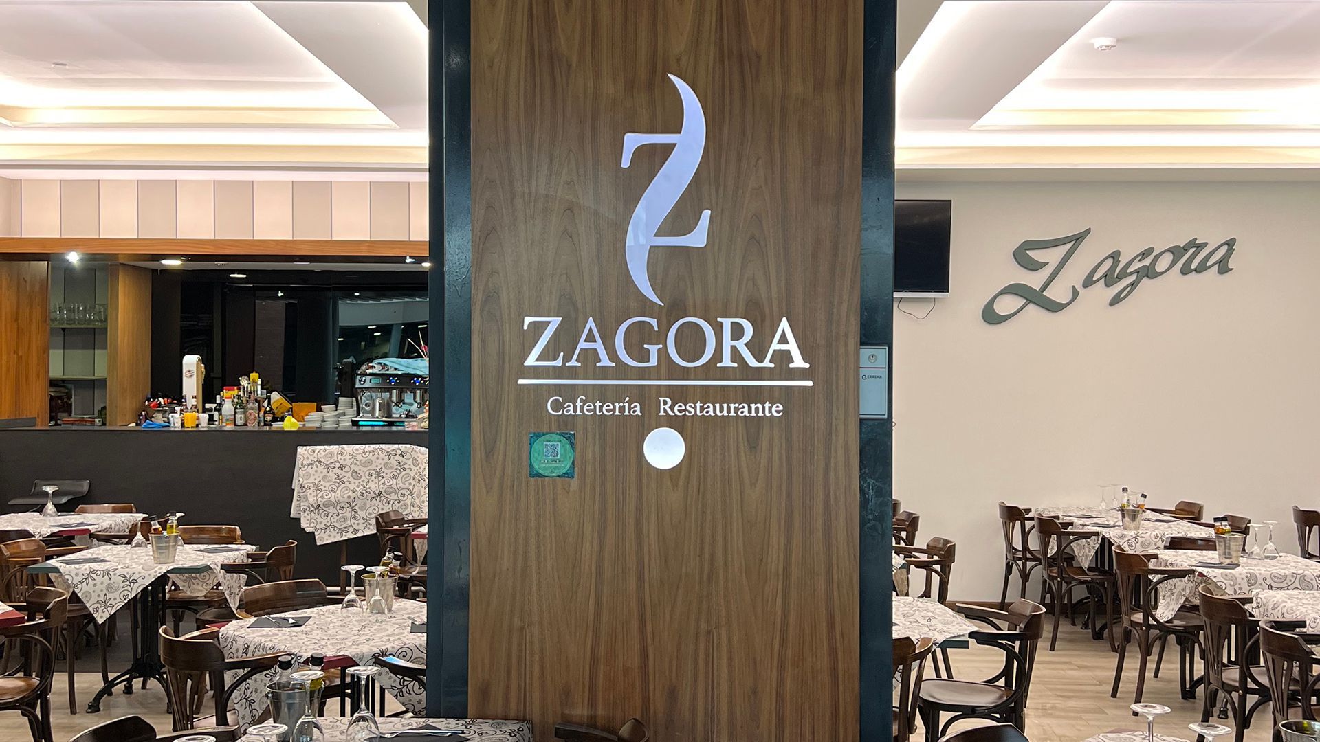 Entrada del restaurante Zagora con pilar de madera, mesas preparadas y logotipo.