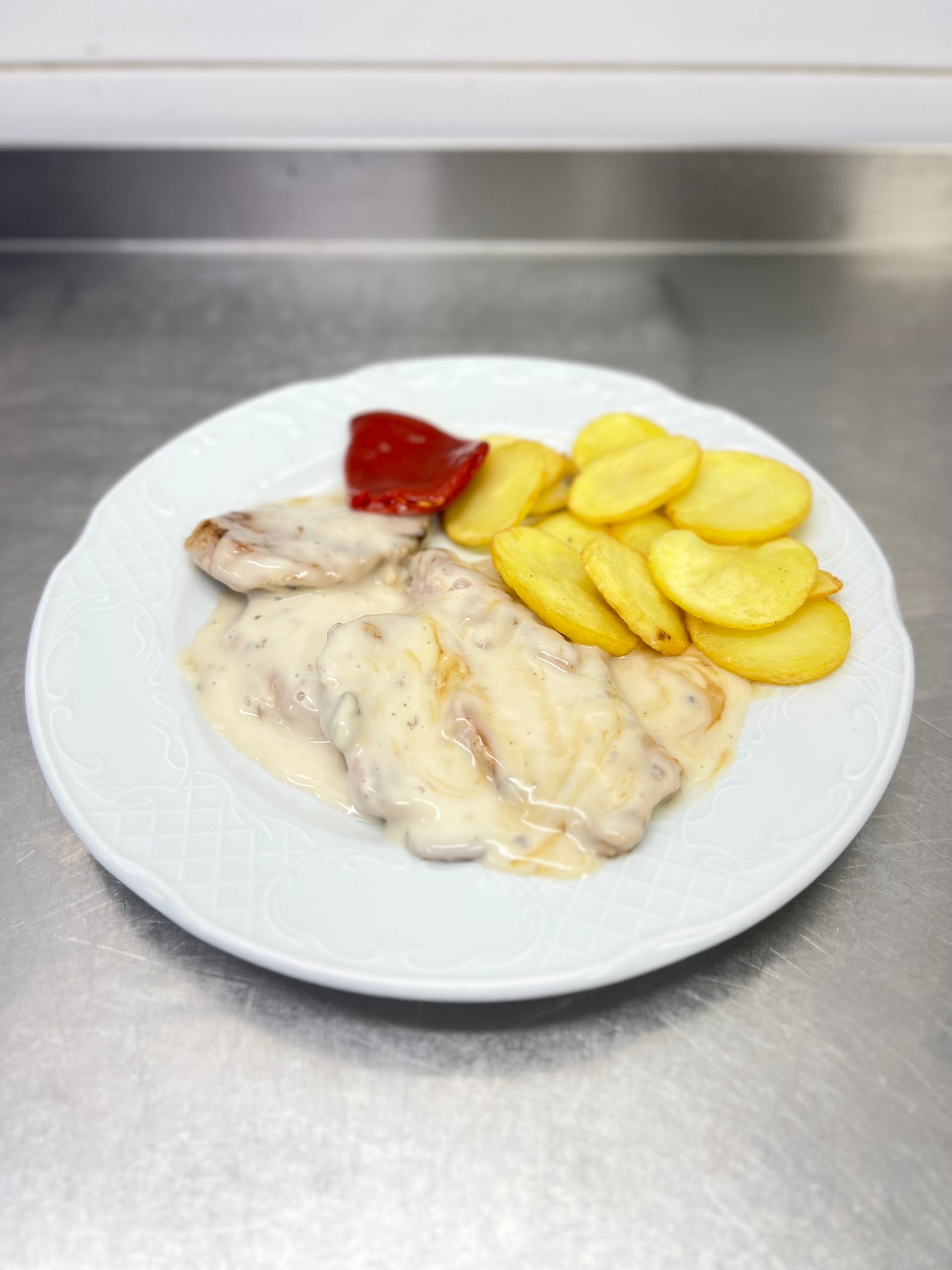 Plato de comida: carne en salsa cremosa con patatas asadas y un pimiento rojo.