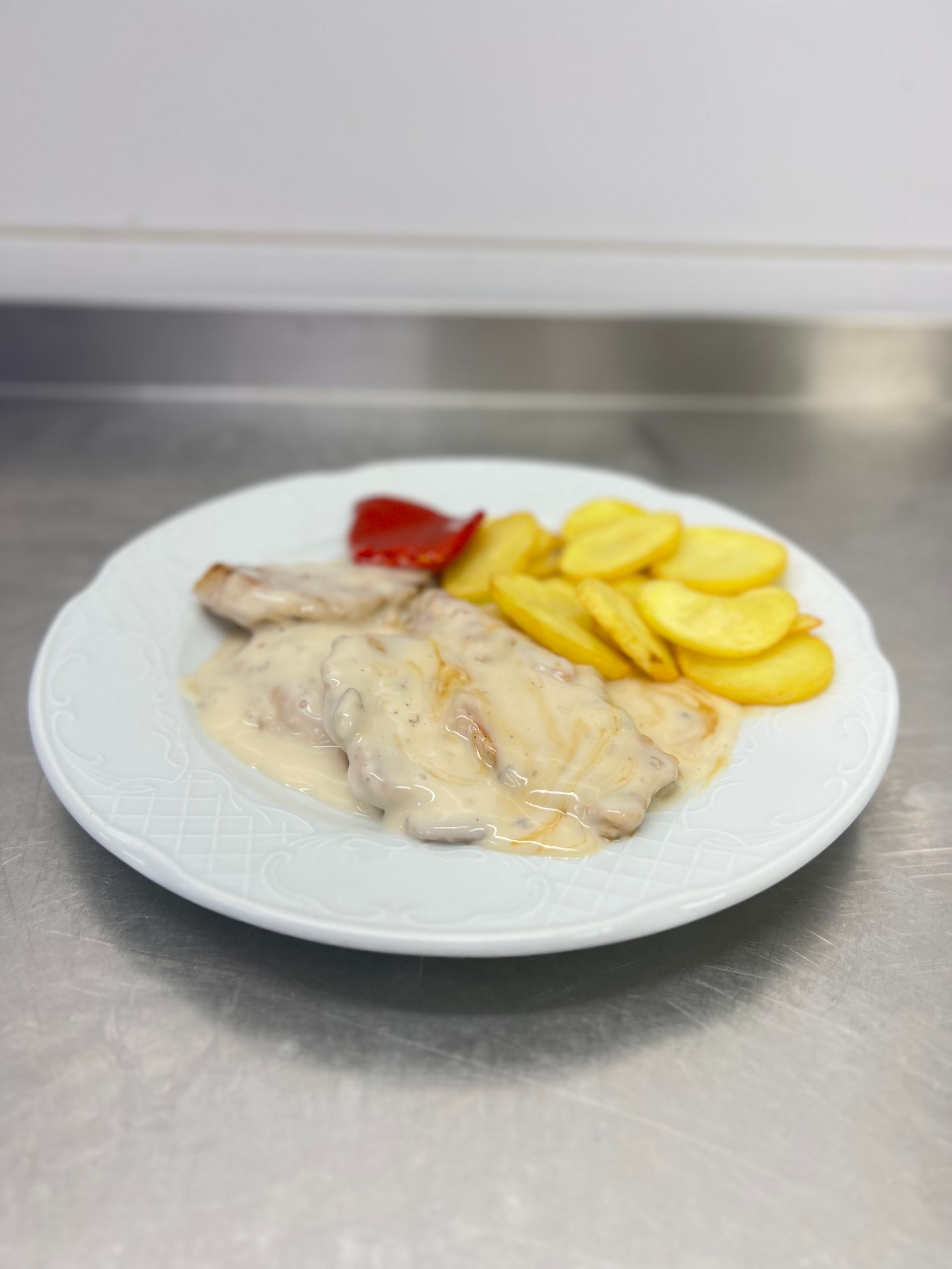 Plato de carne en salsa cremosa con patatas asadas y un trozo de pimiento rojo.