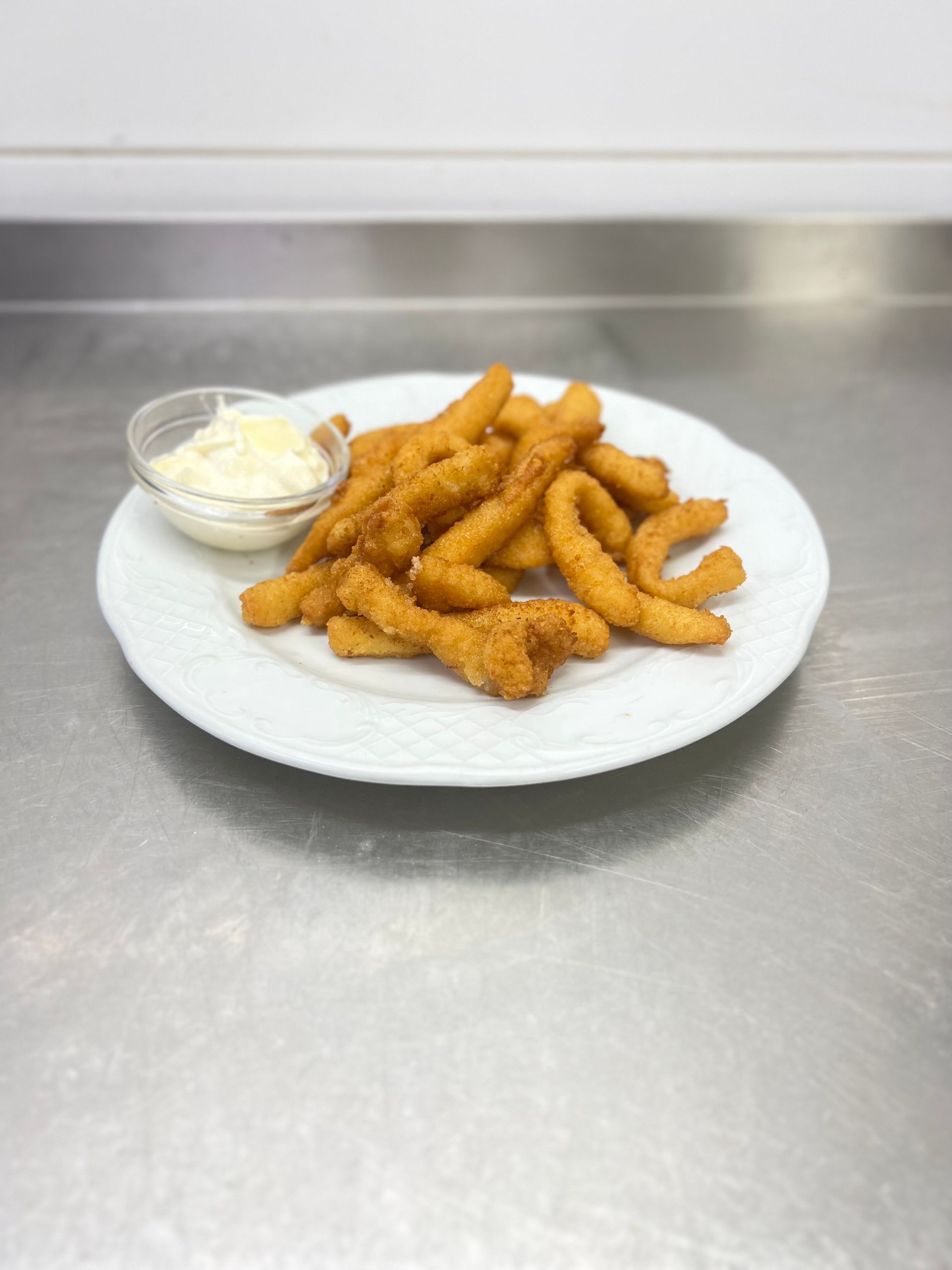 Comida frita y salsa para mojar en un plato blanco, colocado sobre una superficie de acero inoxidable.