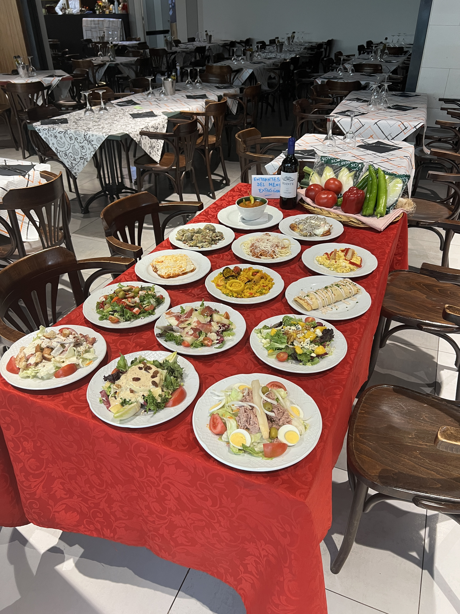 Una mesa repleta de diversos platos preparados, dispuesta en un restaurante con sillas y otras mesas.