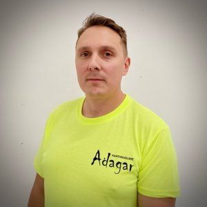 Henkilö seisoo yksinkertaista seinää vasten yllään neonkeltainen mustalla logolla varustettu t-paita.