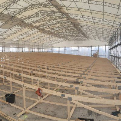 Suuri sisäteltta, jossa on riviä puukehyksiä ja palkkeja betonilattialla