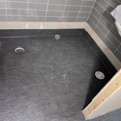 Tyhjä laatoitettu suihkulattia, jossa on tumma allas ja kolme viemäriä ylhäältä katsottuna
