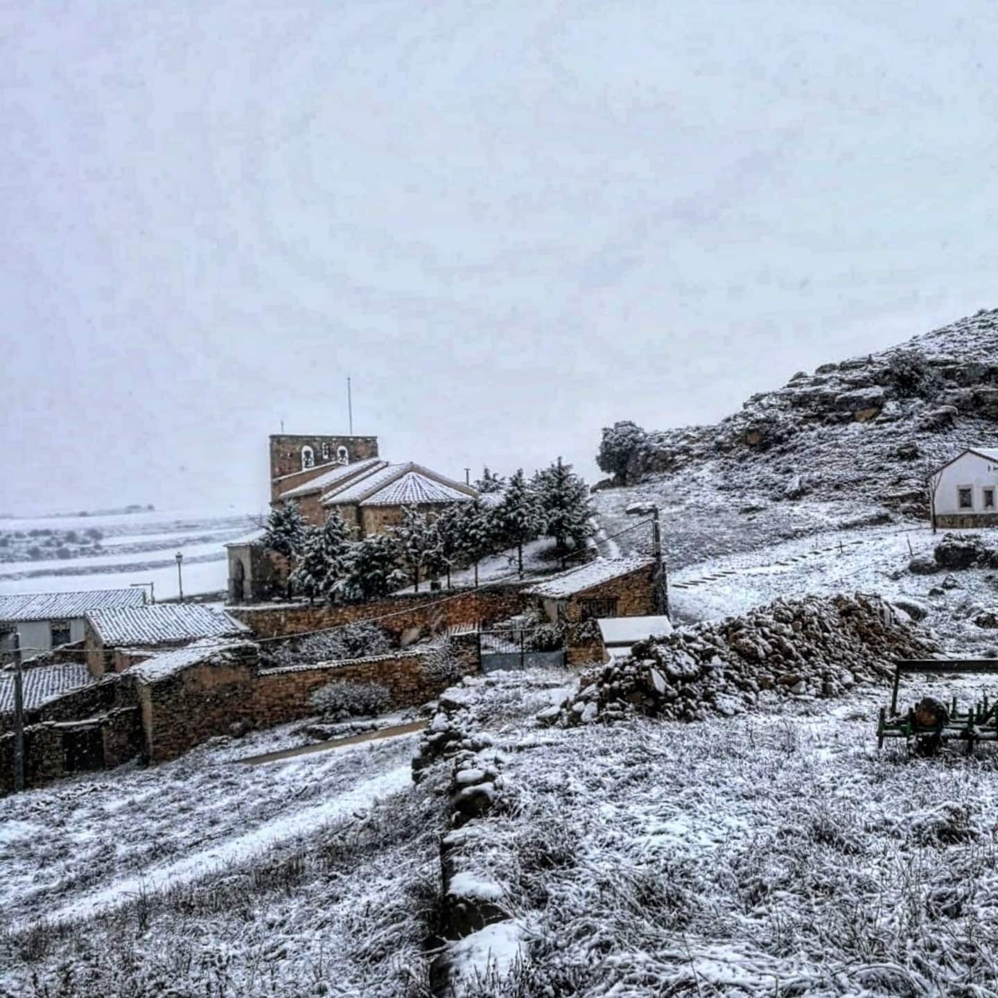 Una ladera nevada con casas y árboles al fondo.