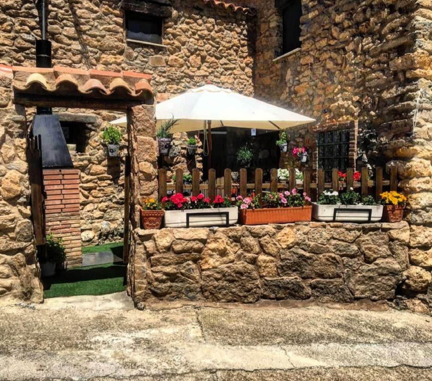 Un edificio de piedra con una sombrilla blanca y flores delante.