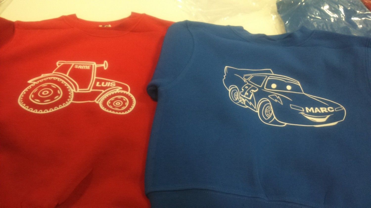 Sudadera roja con gráfico de tractor junto a una sudadera azul con gráfico de un personaje de Cars.