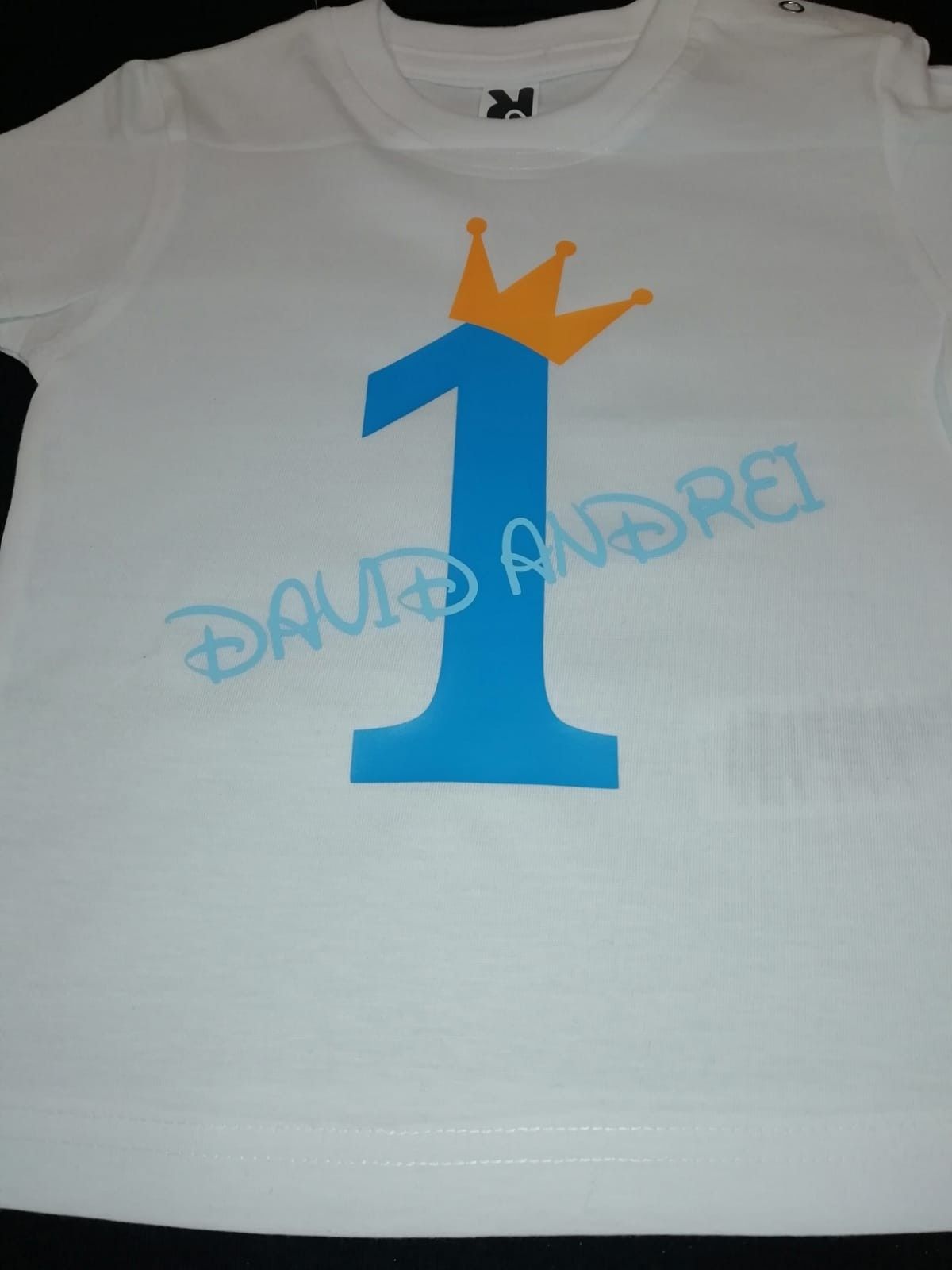 Camiseta blanca con el número uno azul y una corona naranja. Nombre azul 