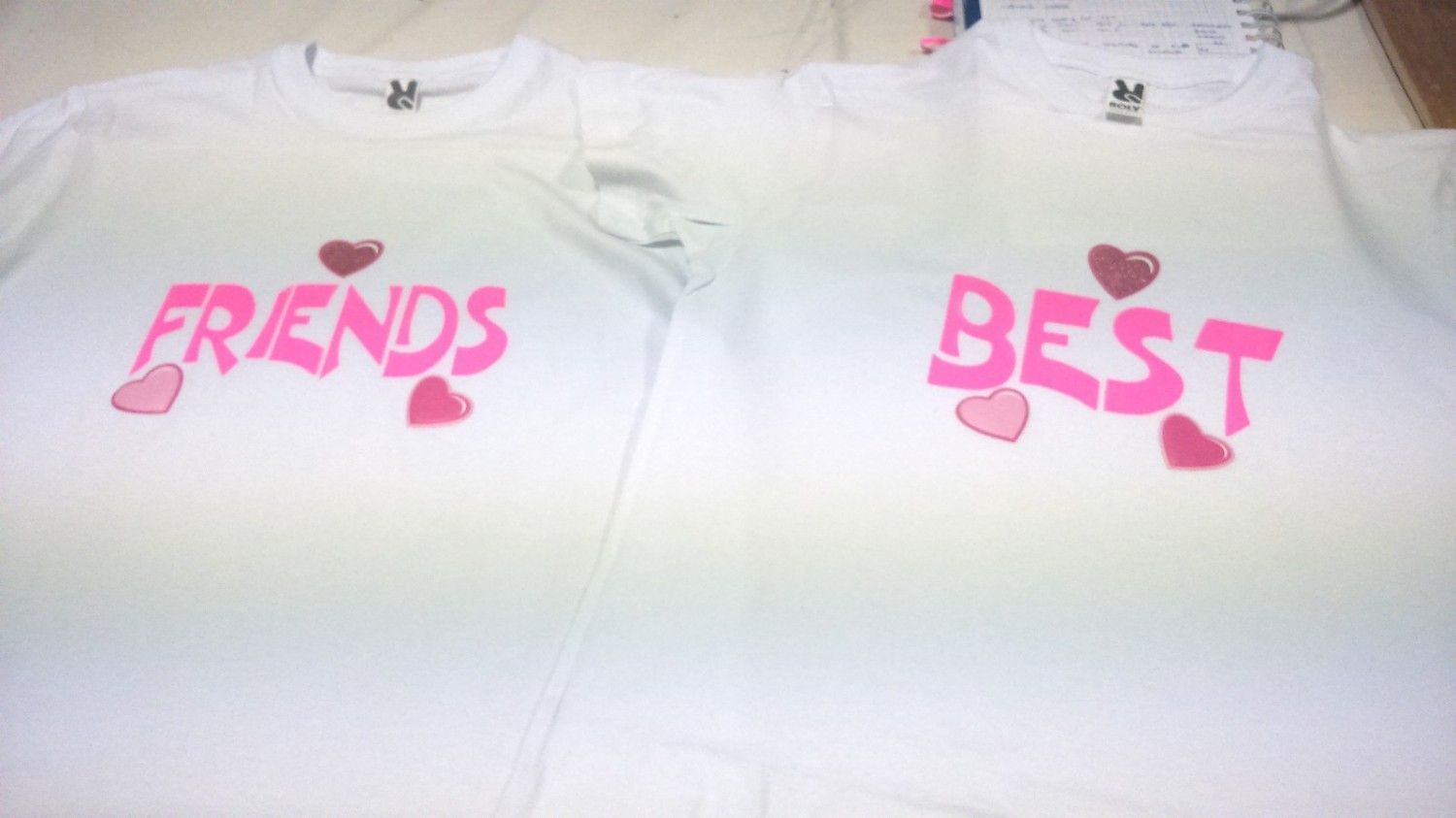 Dos camisetas blancas con texto rosa: “FRIENDS” y “BEST”, decoradas con corazones rosas.