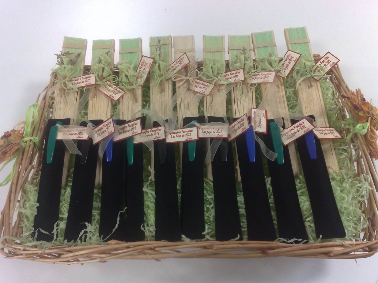 Cesta con bolígrafos en fundas negras, cada una con una etiqueta y detalles decorativos en verde.
