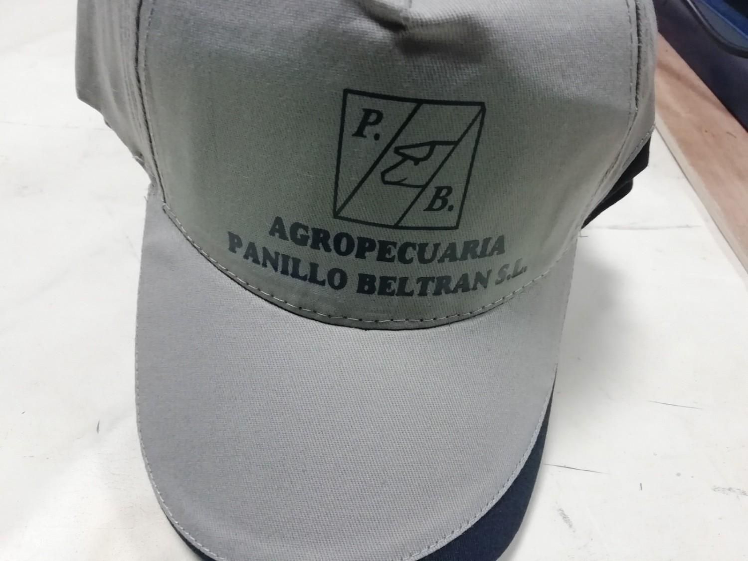 Gorra gris con logo de Agropecuria Panillo Beltran SL, visera azul marino y texto blanco.