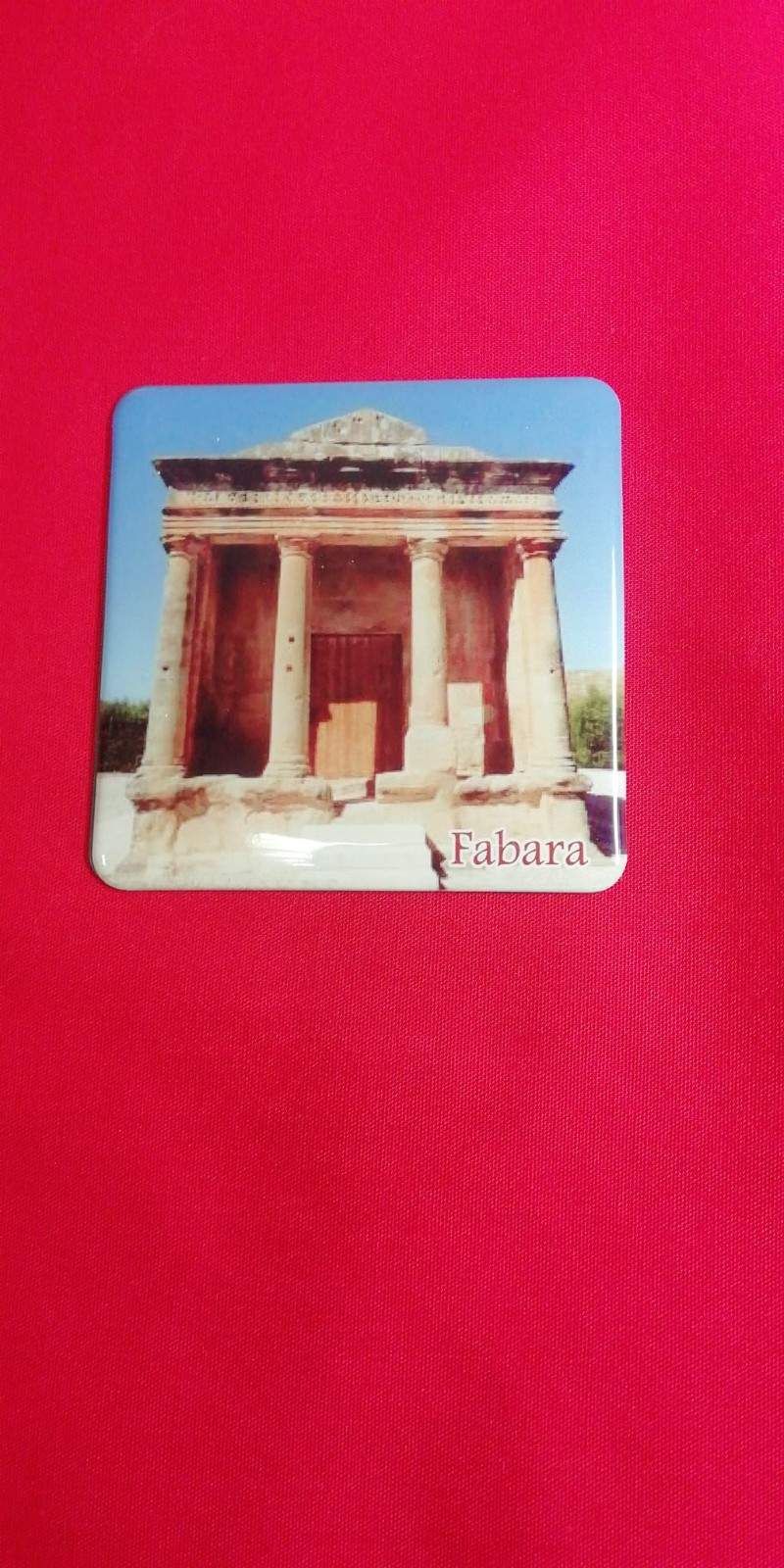 Un imán cuadrado de un antiguo templo con columnas, sobre un fondo de tela roja. Se ve la palabra 