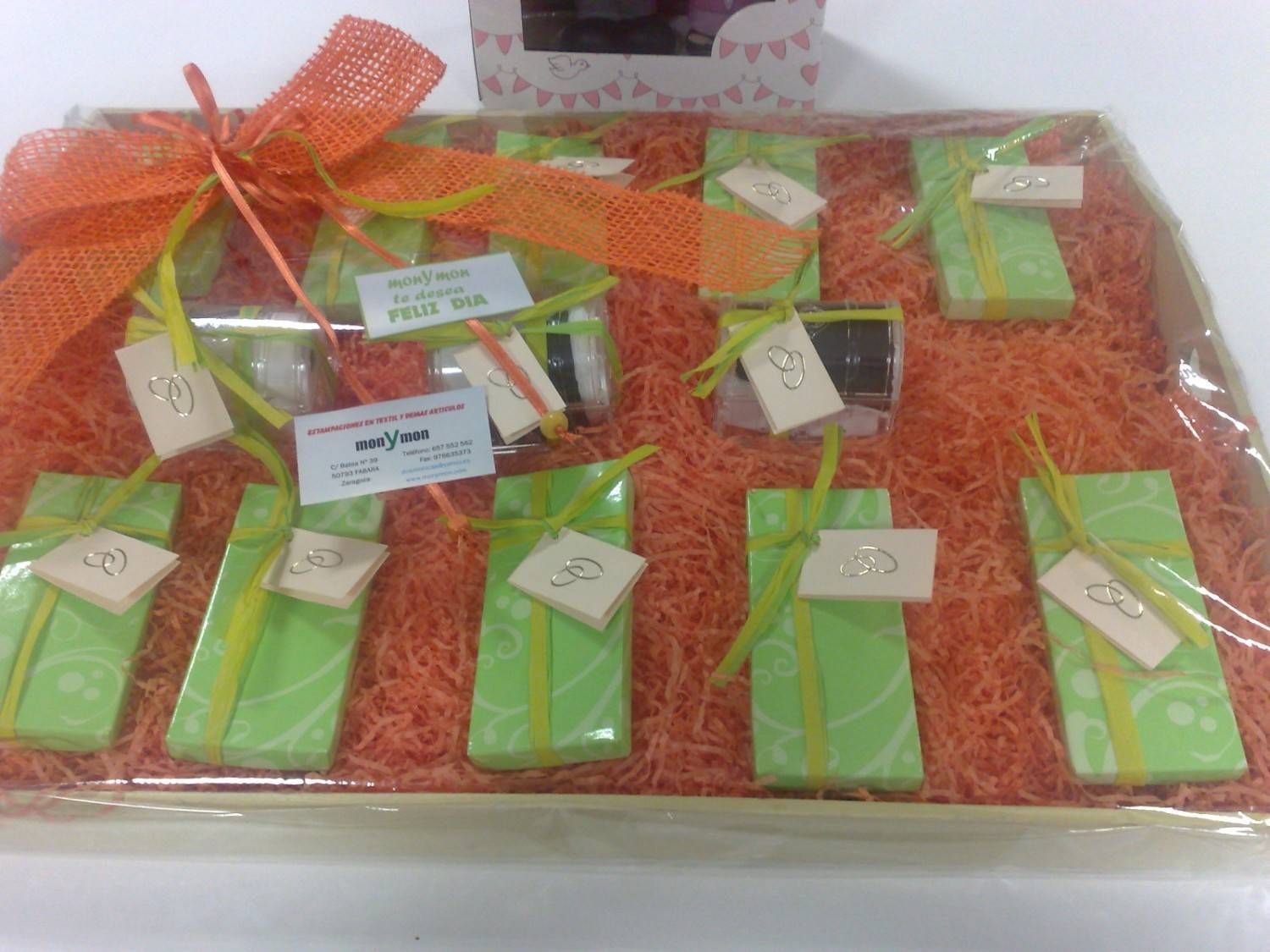 Caja de regalos envueltos en verde, cinta y relleno de color naranja, pequeñas etiquetas.