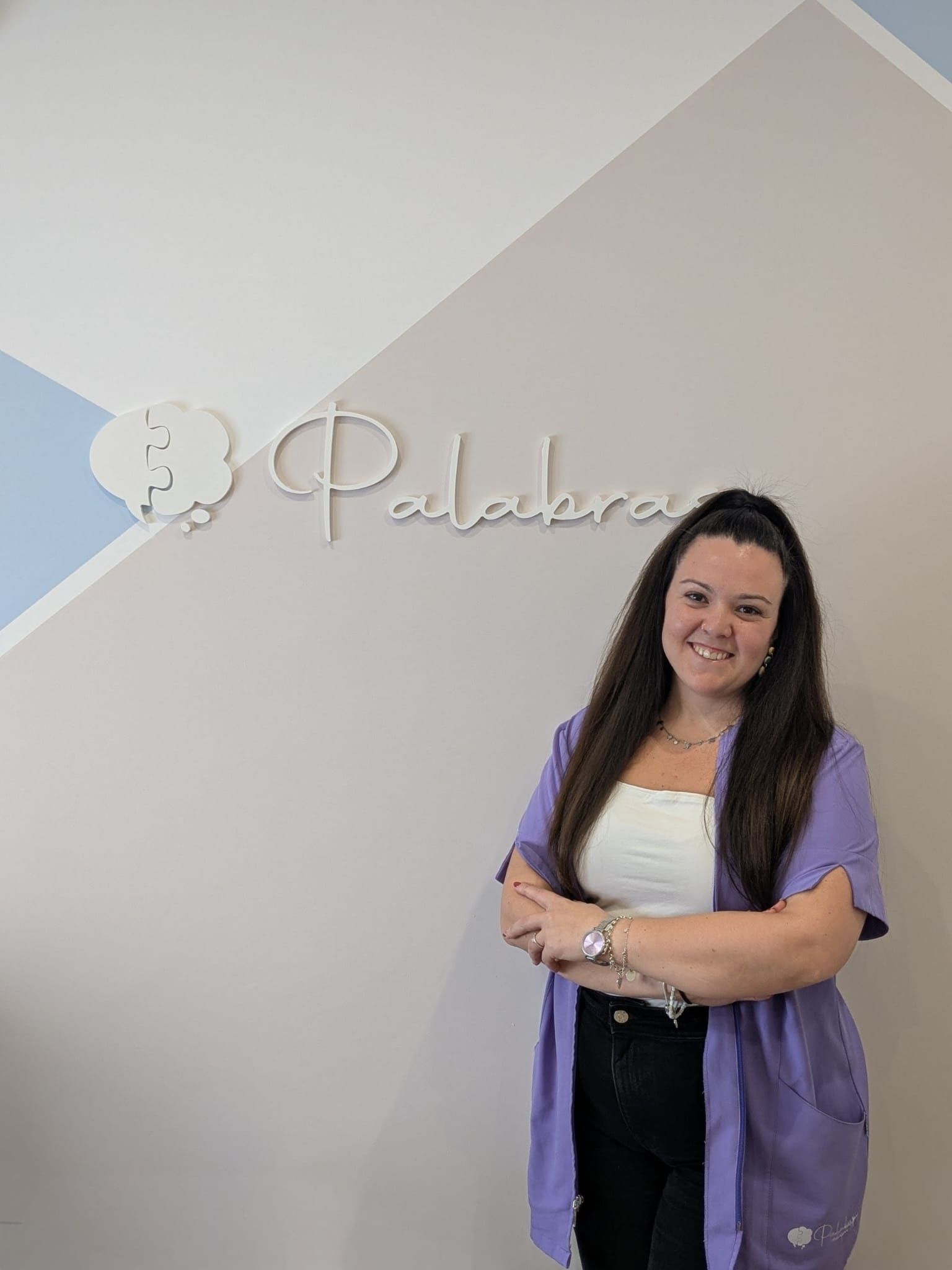 Mujer de pie con los brazos cruzados frente a una pared con un logotipo que dice 