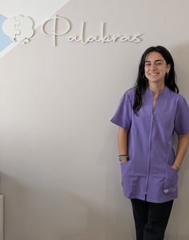 Una mujer vestida con un uniforme médico morado está de pie junto a una pared con la palabra