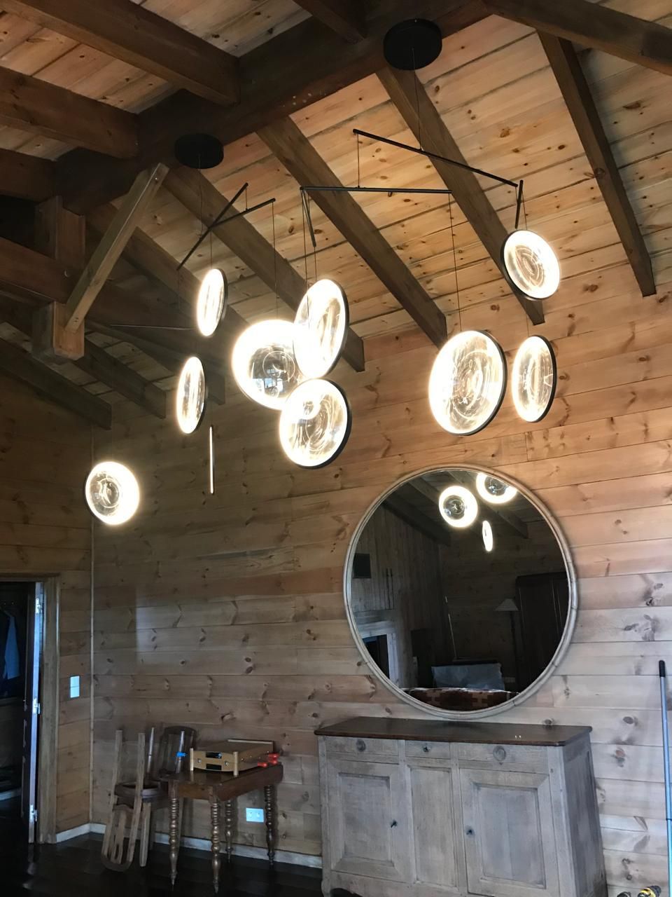 Lustre moderne avec des lumières circulaires et scintillantes se reflétant dans un miroir rond, sur un mur lambrissé.