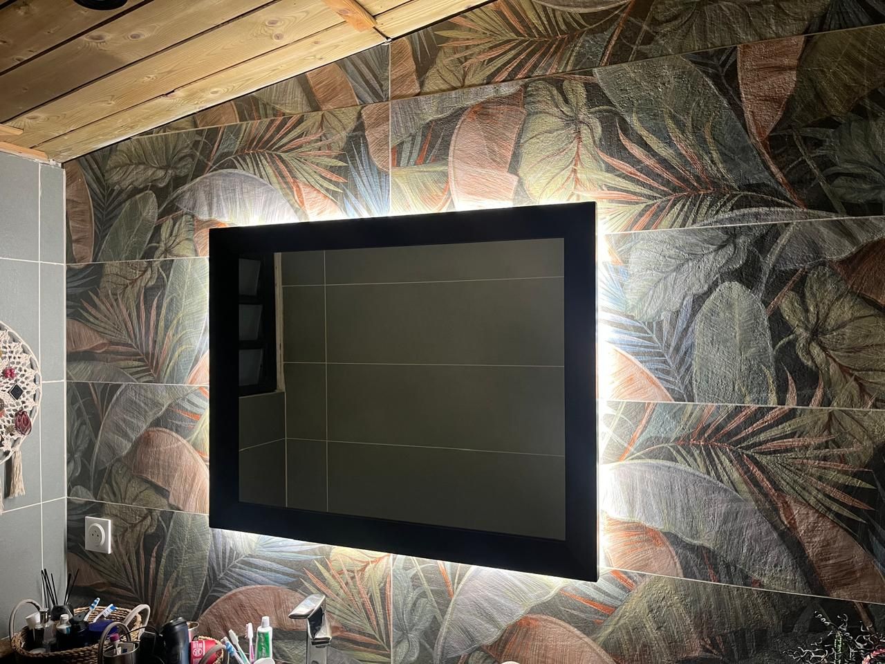 Miroir avec éclairage LED sur un mur carrelé à motifs dans une salle de bain.