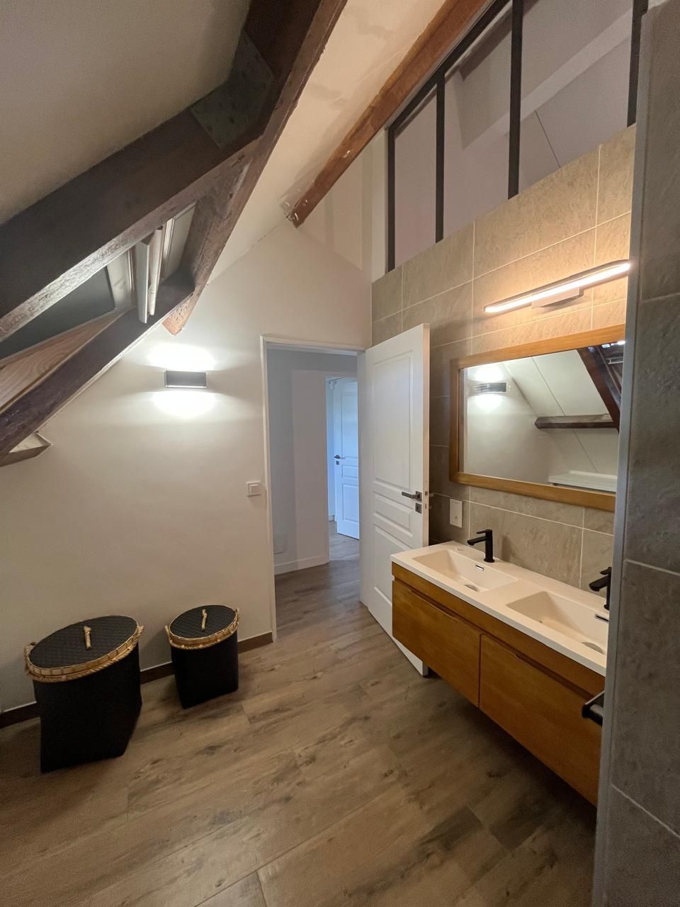 Salle de bains avec éléments en bois, double vasque et poutres apparentes au plafond.