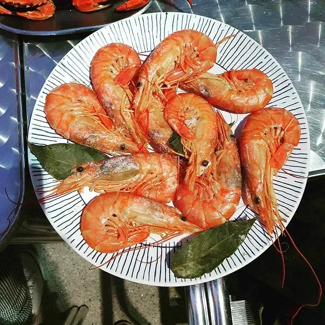 Un plato blanco cubierto con camarones y hojas.