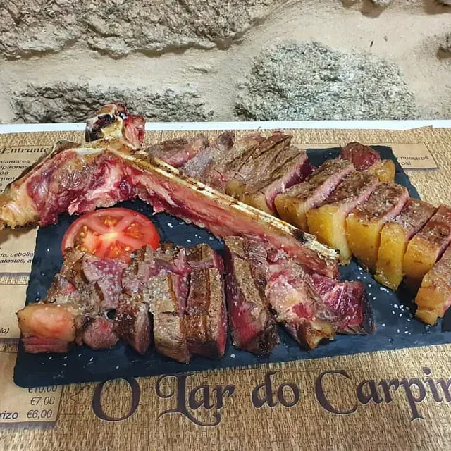 Un plato de carne y patatas está sobre un mantel que dice o lar do carpit