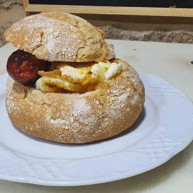 Un sándwich con huevos y salchicha en un plato blanco.