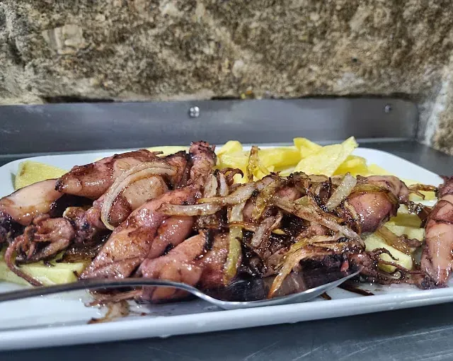 Un plato blanco cubierto con calamares y patatas fritas con un tenedor.