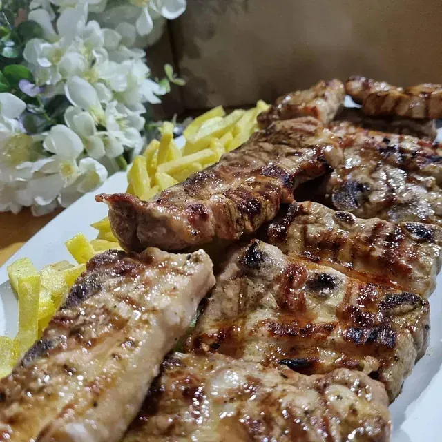 Un plato blanco cubierto con carne a la parrilla y papas fritas.