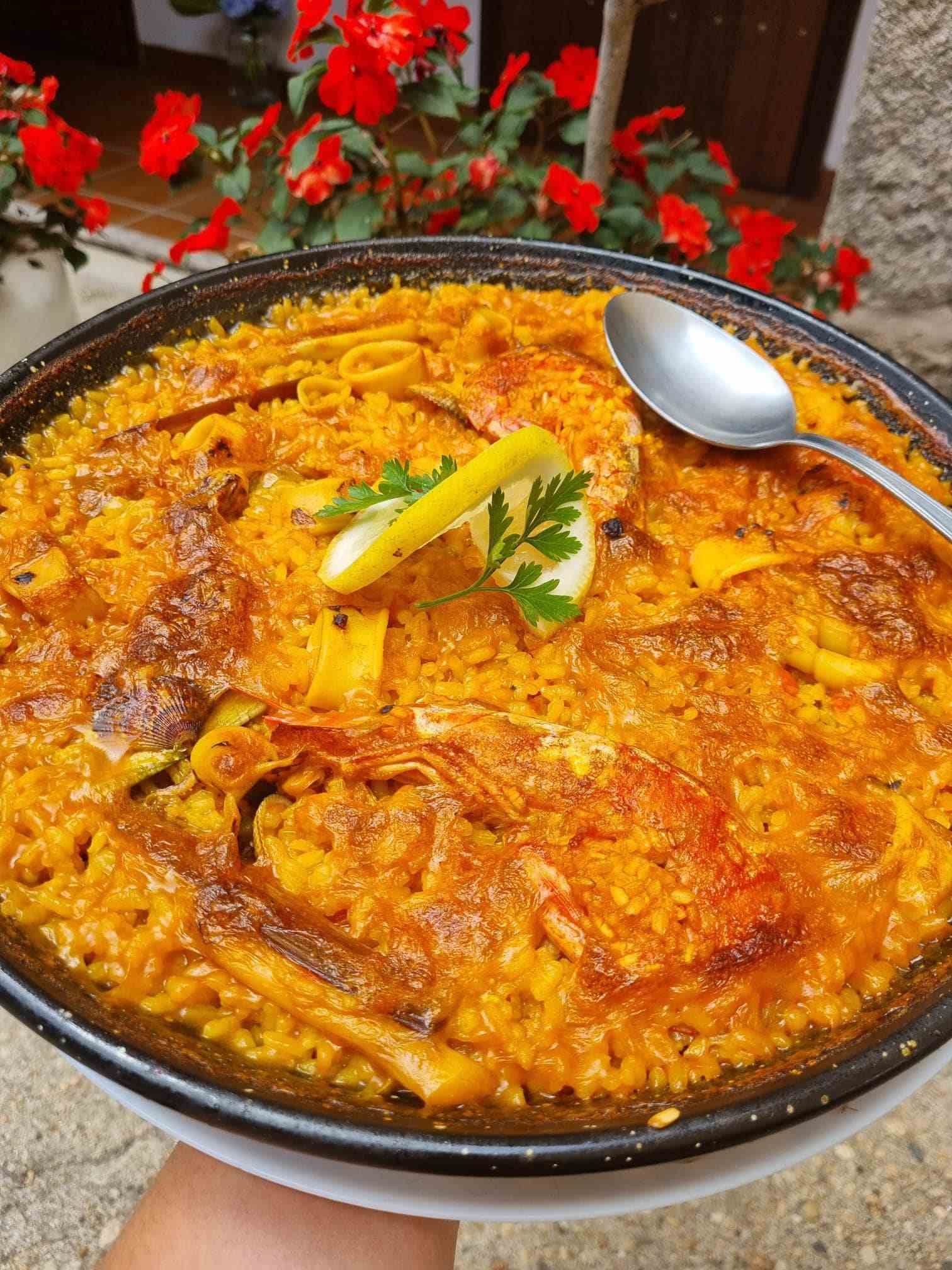 Una persona sostiene una sartén con paella y una cuchara dentro.