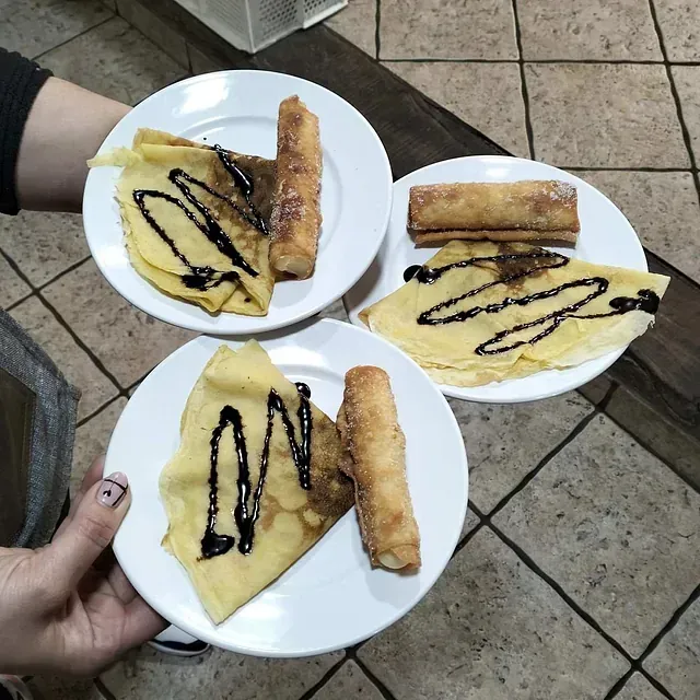 Una persona sostiene tres platos de comida, uno de los cuales tiene un crepe encima.