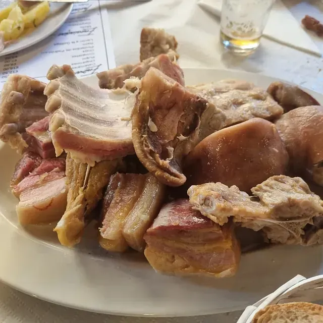 Un plato blanco cubierto con carne y pan sobre una mesa.
