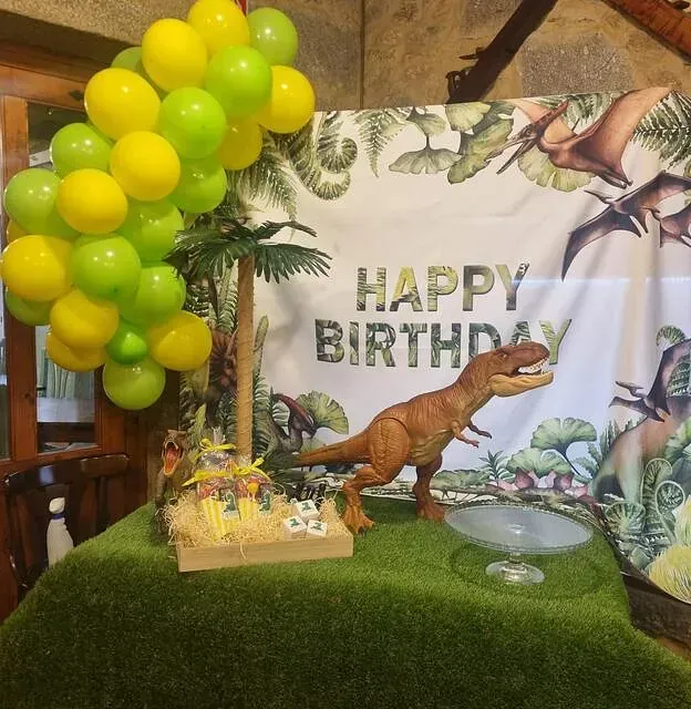 Un cartel de feliz cumpleaños con globos y un dinosaurio de juguete.