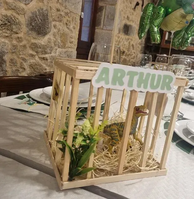 Una jaula de madera con un dinosaurio dentro y un cartel que dice Arthur.