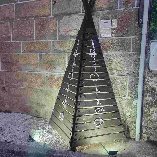 Un tipi de madera está iluminado frente a una pared de ladrillos.