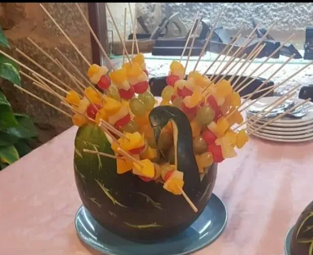 Una sandía llena de fruta y palitos sobre una mesa.