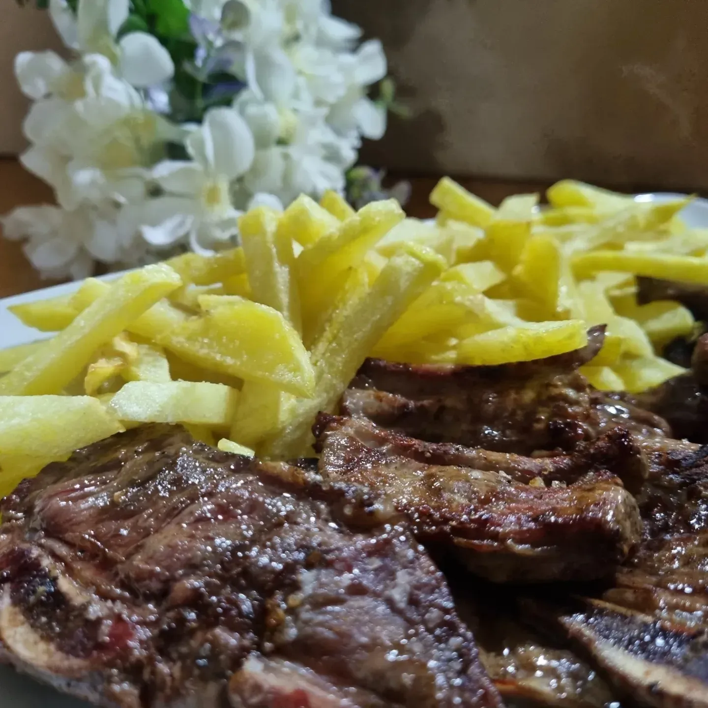 Un plato de carne y patatas fritas con flores de fondo.