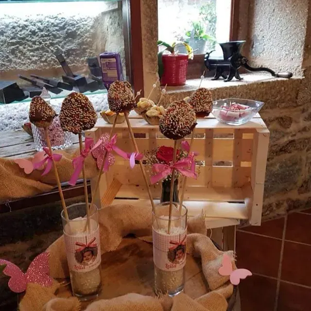 Una mesa con un montón de pastelitos en palitos dentro de vasos que dicen 'cupcakes'.