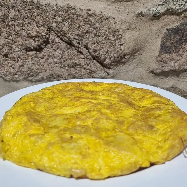 Una tortilla amarilla está en un plato blanco delante de una pared de piedra.