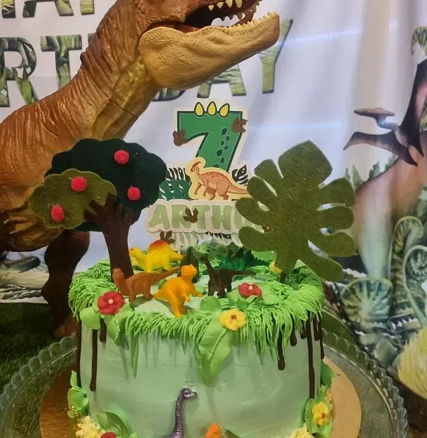 Un pastel de cumpleaños con un T-Rex encima.