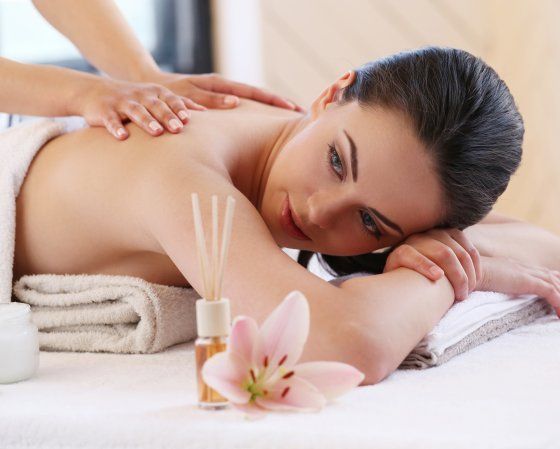 Une personne recevant un massage du dos dans un spa, avec un lys et un diffuseur d'huiles essentielles au premier plan.