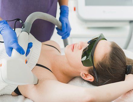 Dans une clinique, un praticien portant des gants bleus utilise un appareil d'épilation laser sur l'aisselle d'une personne.