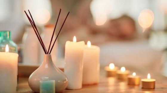 Une scène de spa avec des bougies piliers et des bougies chauffe-plat allumées entourant un diffuseur d'encens, avec une table de massage floue en arrière-plan.