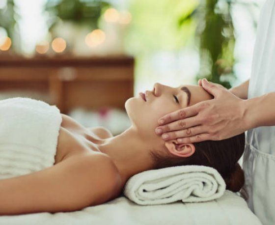 Une personne recevant un massage facial relaxant dans un spa, les mains d'un thérapeute touchant délicatement son visage.