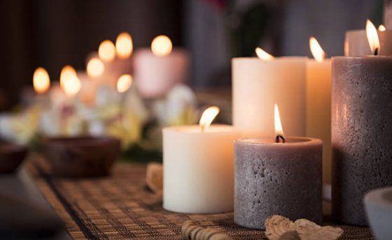 Une collection de bougies piliers lumineuses dans différentes nuances de crème et de gris, disposées sur une table texturée avec des fleurs.