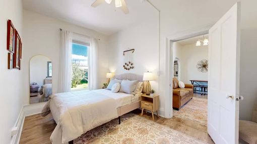 Bright white bedroom with twin beds, patterned rug, arched mirror, and open door to adjoining room