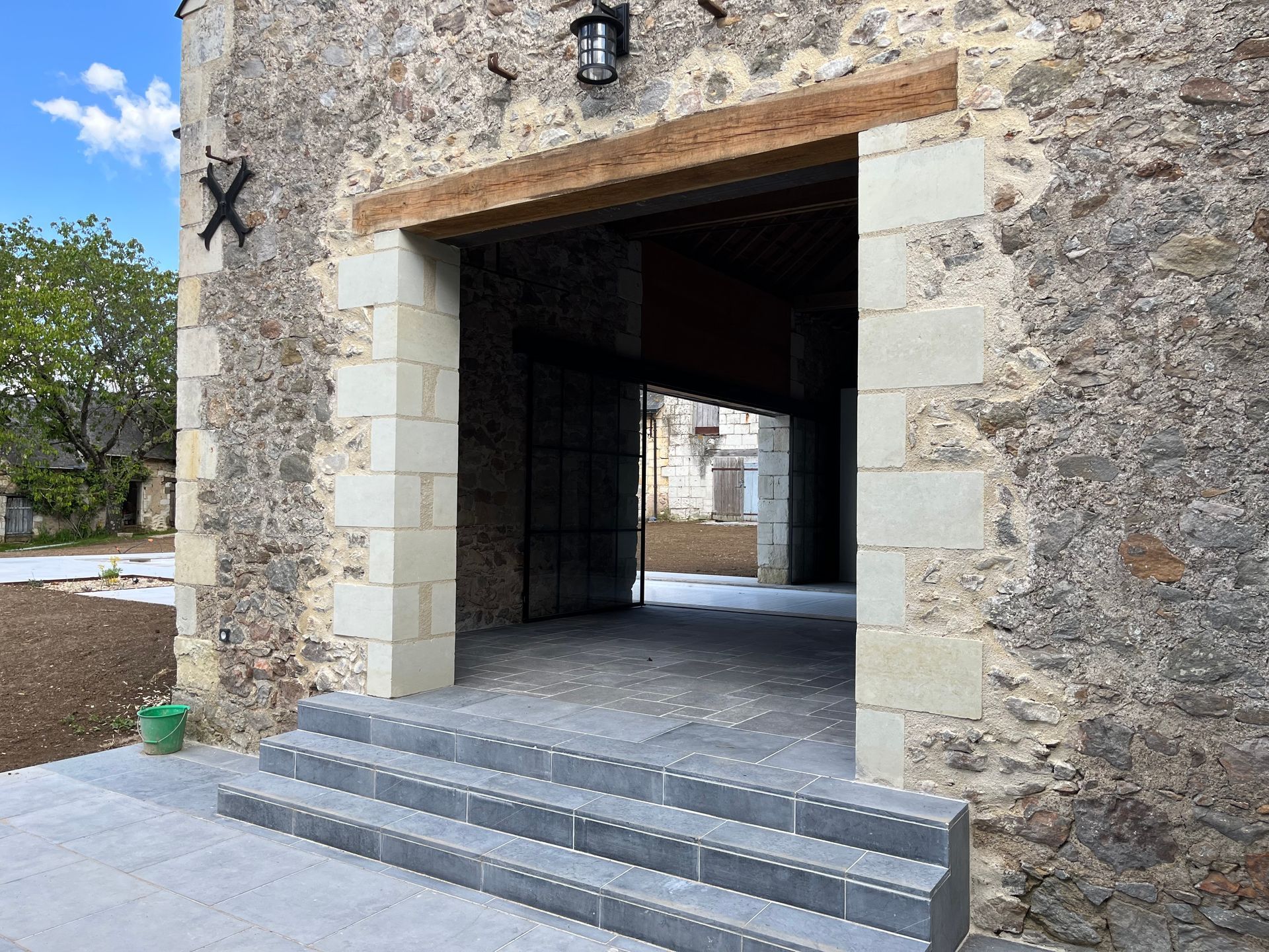Entrée d'un bâtiment en pierre avec trois marches grises menant à une porte ouverte encadrée de blocs de pierre claire.