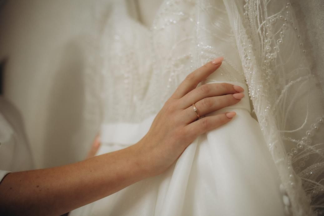 Mano apoyada sobre un vestido blanco con delicada tela transparente.