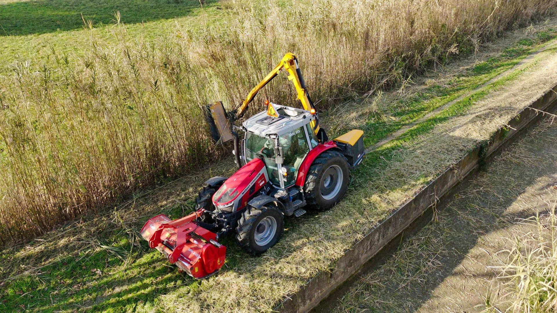Tracteur équipé d’un bras de débroussaillage et d’un broyeur rouge en action pour l’entretien des espaces verts et fossés à Morières-lès-Avignon.